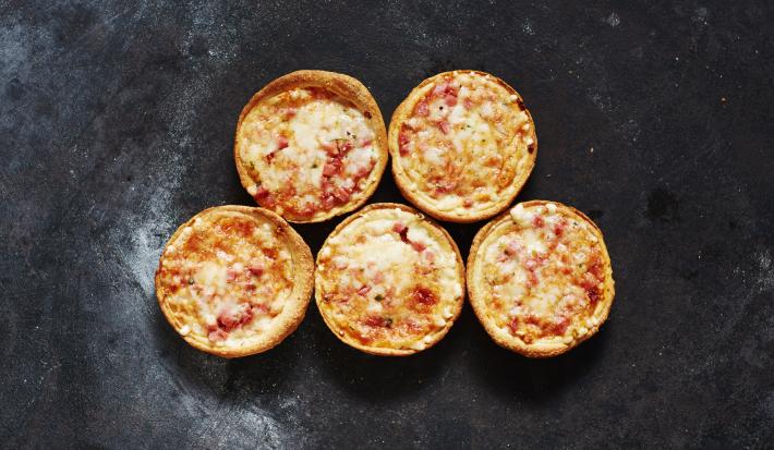 Fotografia vista de cima de cinco mini pizzas de mozarela sobre uma bancada preta com um pouco de farinha.