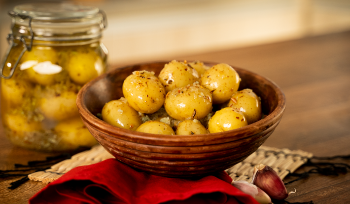 Foto da receita de Batata Bolinha em Conserva. Na foto, observa-se as batatas em um recipiente redondo e, a fundo, um pote hermético transparente com as batatas na conserva.