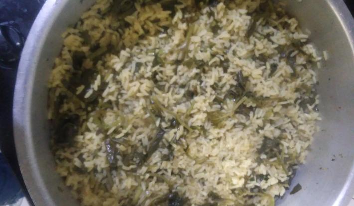 Fotografia vista de cima de uma panela grande de alumínio com arroz de jambu.