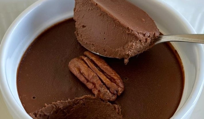 Fotografia de alguns ramkins brancos com mousse de chocolate. O mousse do centro da foto tem uma castanha decorando e uma colher tirando a porção da mousse.
