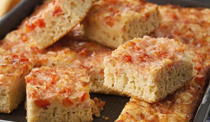 Fotografia em tons de marrom e vermelho em uma bancada de madeira com um recipiente retangular com vários pedacinhos de torta de bauru.