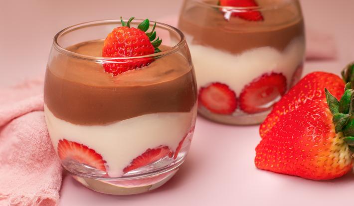 A fotografia mostra camadas de creme branco, ganache de chocolate brilhante e morangos frescos cuidadosamente decorados