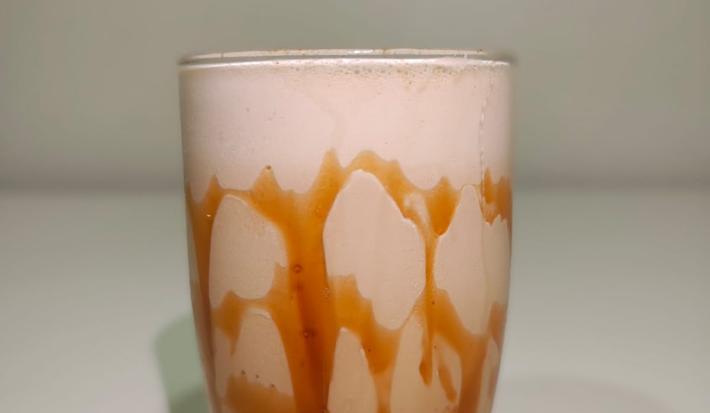 Foto da receita de nescafé caramelo gelado servida no copo de vidro alto sobre uma mesa branca