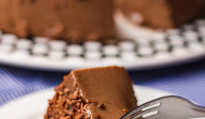 Imagem de um prato branco com uma fatia de brigadeirão Moça com chocolate granulado e um grafo tirando um pedaço.