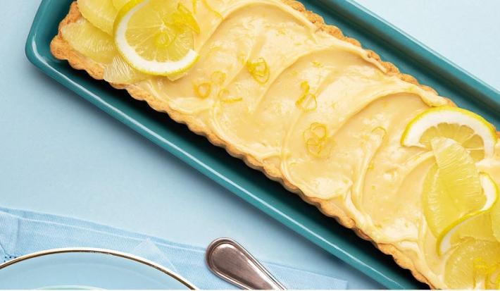 fotografia e tons de azul e amarelo tirada de cima de uma bandeja azul com a torta e rodelas de limão por cima