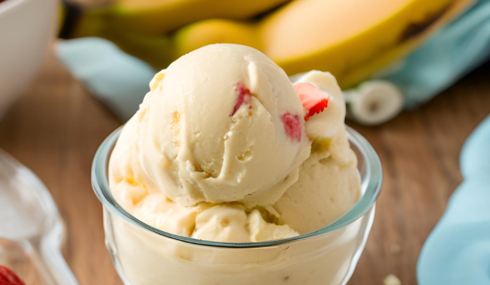 Foto da receita de Sorvete de Banana com Morango. Observa-se uma tacinha de vidro com as bolas de sorvete dentro, na cor amarela e com pedacinhos de morango. Foto gerada por IA.