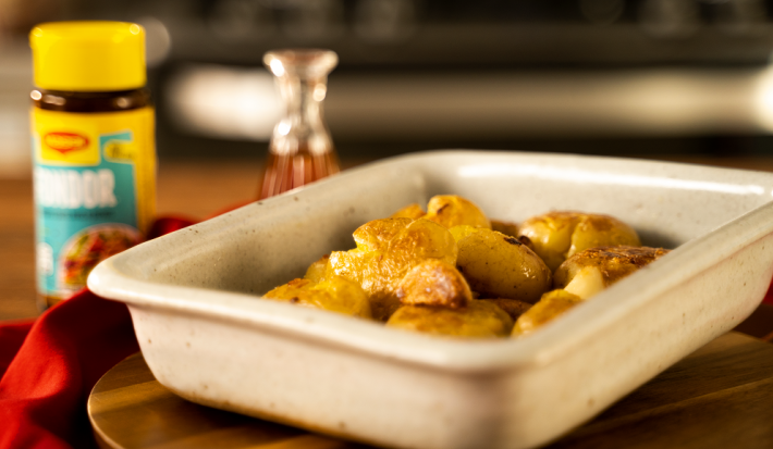 Foto da Receita de Batata Bolinha ao Murro. Observa-se um recipiente refratário de cerâmica com as batatas em cima de uma tábua de madeira. Ao fundo, um pote de Maggi Fondor.
