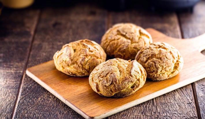 Foto da receita de broa de milho servida em quatro porções sobre uma tábua de madeira em cima de uma mesa de madeira escura