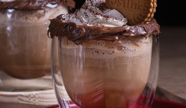 Foto da receita de cappuccino avelã servida em dois copos de vidro com um biscoito em cima