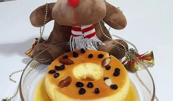 Foto da Receita de Pudim de Leite Moça Com Amêndoas e Passas. Observa-se um pudim em uma travessa redonda de vidro e festivo, decorado com uma rena de Natal!