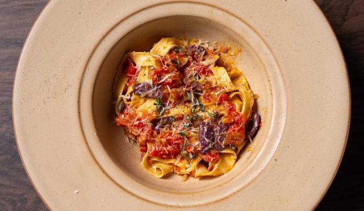 Fotografia em tons de bege com um prato de macarrão talharim ao centro. Por cima do macarrão existe um molho de tomates com anchovas e alcaparras.