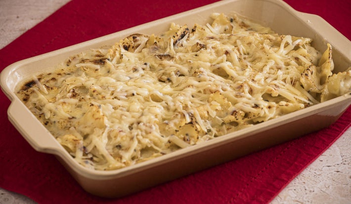 Foto bem aproximada da receita de Macarrão gratinado com queijo Tirolez, servida em uma travessa marrom, sobre um pano vermelho. O macarrão está levemente gratinado por cima