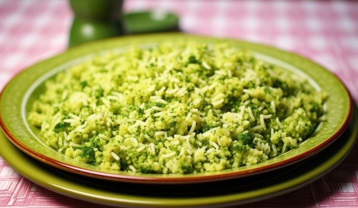 Em cima de uma mesa, prato redondo com porção de arroz soltinho verde e brócolis picados.