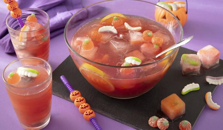 Foto da receita de ponche de halloween sem álcool servida em um recipiente de vidro grande com decoração de halloween em volta