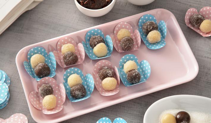 Foto da receita de Brigadeiro de Cappuccino. Observa-se uma travessa retangular rosa clara com 9 brigadeiros sobre forminhas rosas e azuis com estampa de poá.