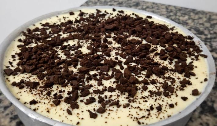 Fotografia de uma forma de alumínio redonda e grande com uma receita de pavê delícia de limão com kitkat branco e negresco por cima.