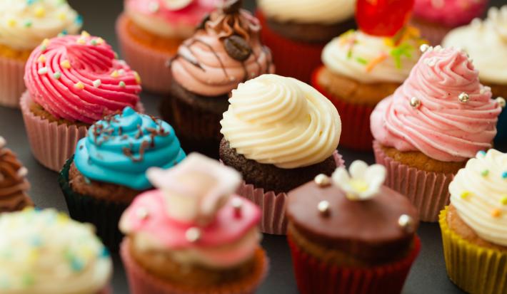 Fotografia de várias unidades de forminhas com cupcakes diversos coloridos e confeitados sobre uma mesa preta.