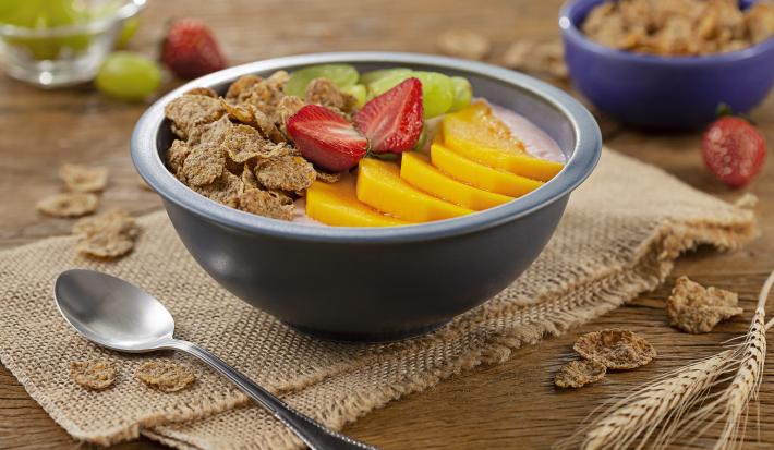 Foto de uma tigela na cor azul com o Poke de Iogurte dentro e decorado com cereais, morango, uvas