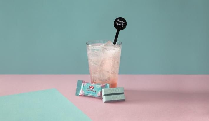 Foto da receita de Soda Italiana Bubble Gum. Observa-se um fundo azul bebê com o copo alto ao centro, com xarope de chiclete e servido com KIT KAT Cotton Candy