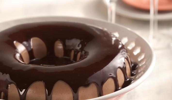 em um recipiente branco e redondo contém uma cassata de chocolate com cobertura de chocolate por cima.