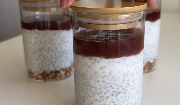 Fotografia mostra potes individuais de cheesecake, com camadas visíveis de granola, creme claro com chia e cobertura de geleia vermelha.