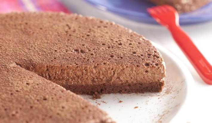 fotografia em tons de azul e marrom tirada de uma torta de chocolate com uma fatia retirada, e ao fundo um prato redondo azul com um pedaço da torta
