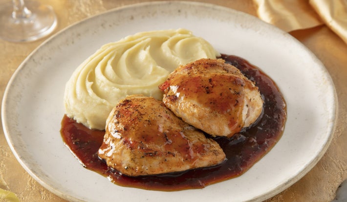 Pedaços de frango dourados servidos com purê cremoso de batata e molho escuro reduzido, apresentados em prato branco elegante