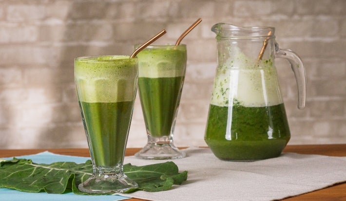 Fotografia em tons de verde com dois copos grandes ao centro. Dentro dos copos existe uma receita de suco verde feita com couve e Molico.