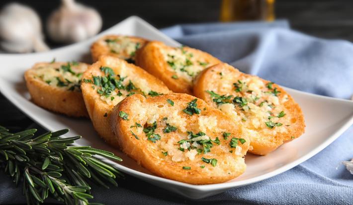 Fotografia em tons de branco com um prato branco ao centro. Em cima do prato existe uma receita de rabanada salgada com ervas e queijo parmesão