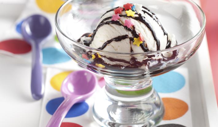 fotografia em tons de rosa e branco tirada de uma bandeja branca com duas taças e ambas contém um bola de sorvete com calda de chocolate.