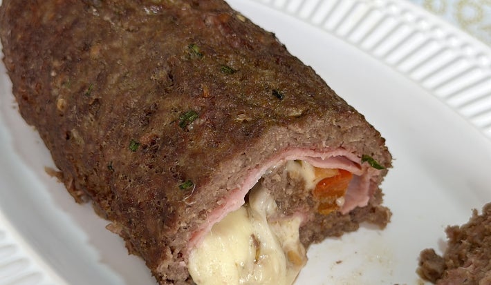 Foto aproximada da receita de rocambole de carne com aveia, cortado, podendo ver o interior com o recheio de presunto e queijo muçarelo bem derretido