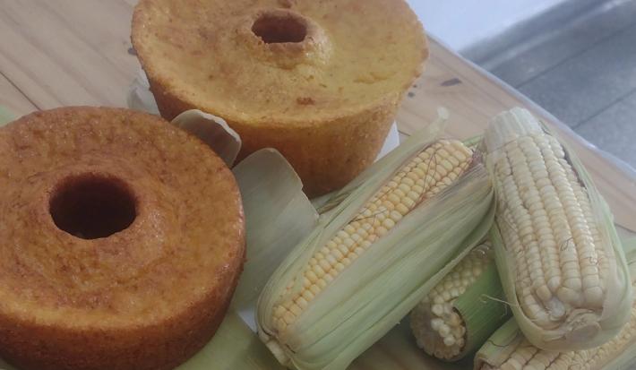 Foto da receita de Bolo de Milho Espetacular. Observa-se dois bolos de milho assados e, ao lado direito, três espigas de milho decorando