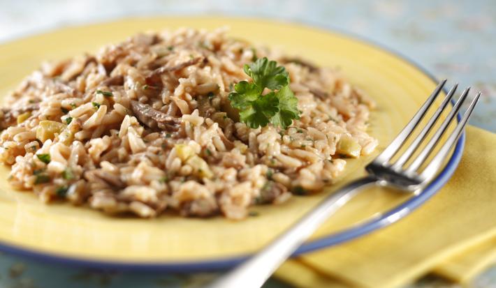 Fotografia em tons de branco e amarelo de uma bancada branca com um paninho amarelo, sobre ela um prato amarelo com risoto e um garfo.