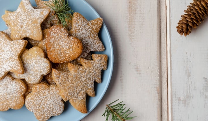 Em cima de uma mesa, prato redondo com biscoitos em formato de árvore de Natal, decorados com açúcar de confeiteiro.
