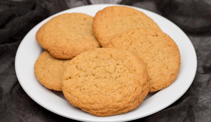 Em cima de uma mesa, prato redondo com porção de biscoitos redondo e dourados.