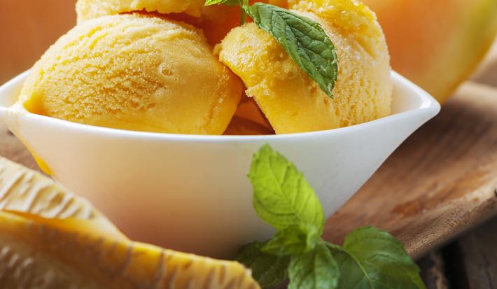 fotografia em tons de marrom e laranja de uma bancada marrom vista de frente, contém um recipiente branco com bolas de sorvete dentro