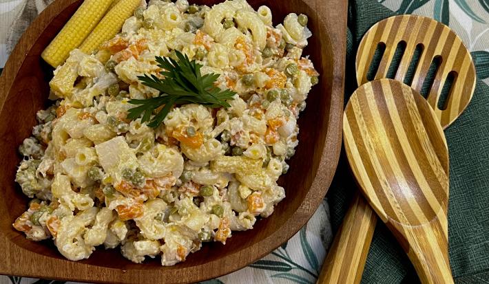Foto da Receita de Macarronese. Observa-se um recipiente de madeira escuro com a macarronese. Ao lado direito, duas colheres grandes de servir.