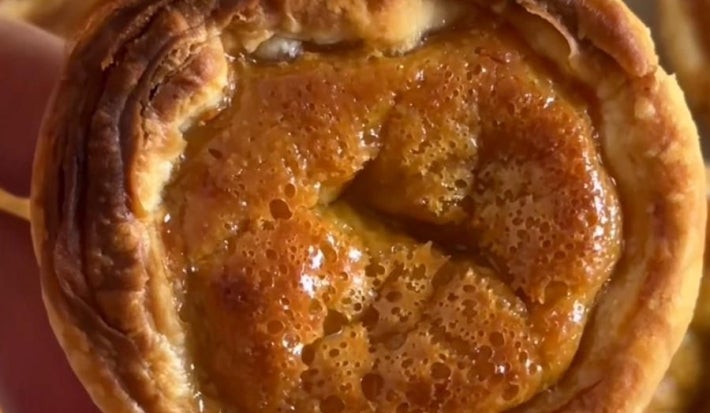 Fotografia de uma mão segurando um pastel de nata no centro da foto. No fundo, atrás do pastel, tem mais unidades.