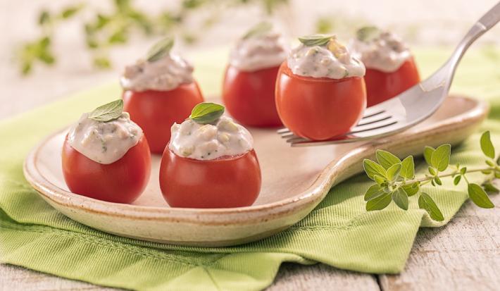 Foto em tons de verde da receita de tomatinho recheado servido em algumas porções em um prato exótico de madeira sobre um pano verde com algumas folhas de decoração