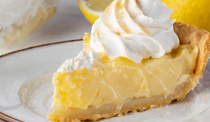 Fotografia de um pedaço de torta de limão com merengue em um prato raso grande.