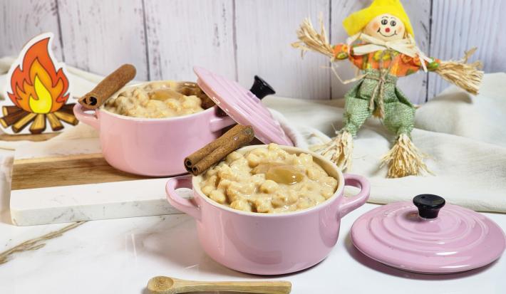 Foto de uma cena com dois potes rosas com a canjica de doce de leite dentro, alguns paus e canela decorado, pequenos espantalhos decorativos ao fundo, tudo sobre uma bancada de mármore branca com tecidos