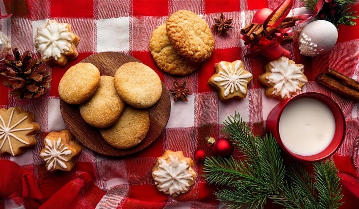 Em cima de uma mesa decorada de Natal, prato com biscoitos redondos e formado de estrelas crocantes, os em formato de estrela estão decorados com glacê branco.