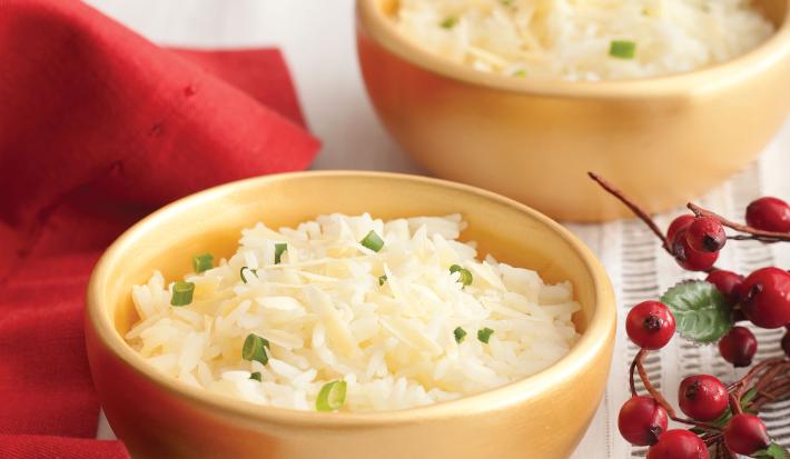 Fotografia em tons de vermelho em uma mesa de madeira com uma toalha branca e um pano vermelho ao lado. Ao centro, um prato fundo dourado com o arroz feito com vinho branco.