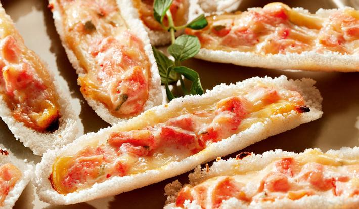 Fotografia em tons de vermelho e bege em uma mesa com um prato redondo raso bege com detalhes e várias barquinhas feitas de tapioca com recheio de tomate.