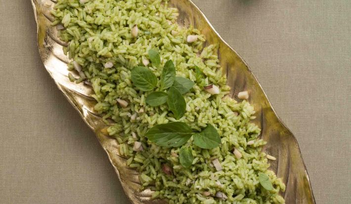 fotografia em tons de cinza, prata e verde de uma bancada cinza vista de cima. Contém um recipiente prata em formato de folha com o arroz.