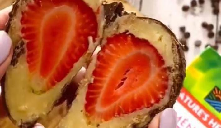 Foto da receita de Bombom de morango. Observa-se um bombom de morango cortado ao meio com o morango e o brigadeiro exposto, com uma mão segurando.