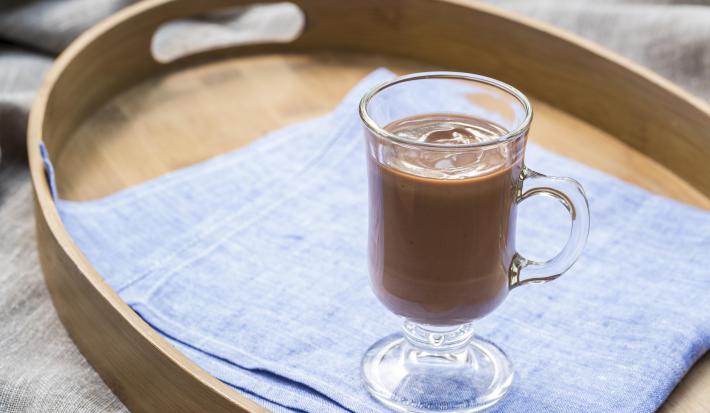 Fotografia em tons de azul e marrom, com bandeja ao centro sobre toalha cinza, dentro um copo com chocolate quente sobre guardanapo azul. Fotografia em tons de azul e marrom, com bandeja ao centro sobre toalha cinza, dentro um copo com chocolate quente sobre guardanapo azul.