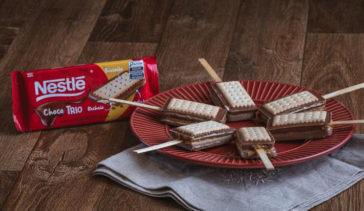 Foto da receita de    Receita de Pirulito de Paçoca com Choco Trio Amendoim. Observa-se 6 pirulitos dispostos em um prato vermelho redondo sobre um pano cinza.