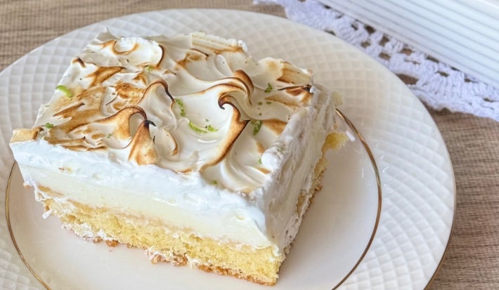 Foto aproximada de uma fatia da receita de Bolo Torta de Limão, com uma camada de bolo branco, outra de recheio e finalizado com merengue levemente maçaricado