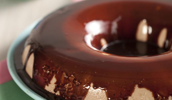 foto em tons de branco e marrom tirada de frente, contém um prato redondo azul com uma sobremesa gelada de chocolate com calda de chocolate por cima